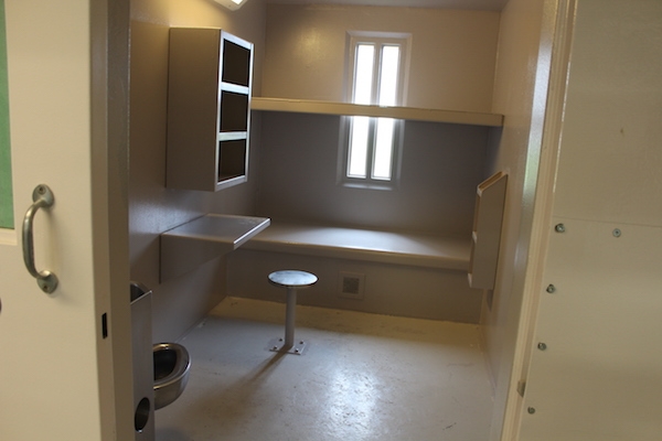The inside of a cell at Central Nova Scotia Correctional Facility in Burnside. It's super small, and everything is painted beige. There are two bunks, one obscuring the small window. There's a tiny table bolted to the wall, and one stool bolted to the floor. The toilet sink combo is in the corner by the door. Very homey.