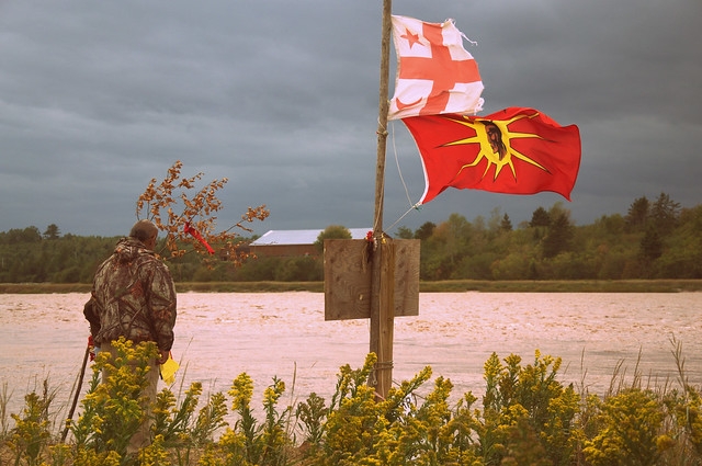 Man by Shubenacadie River at the Alton Gas site, with Mi'kmaq and Warrior flags.