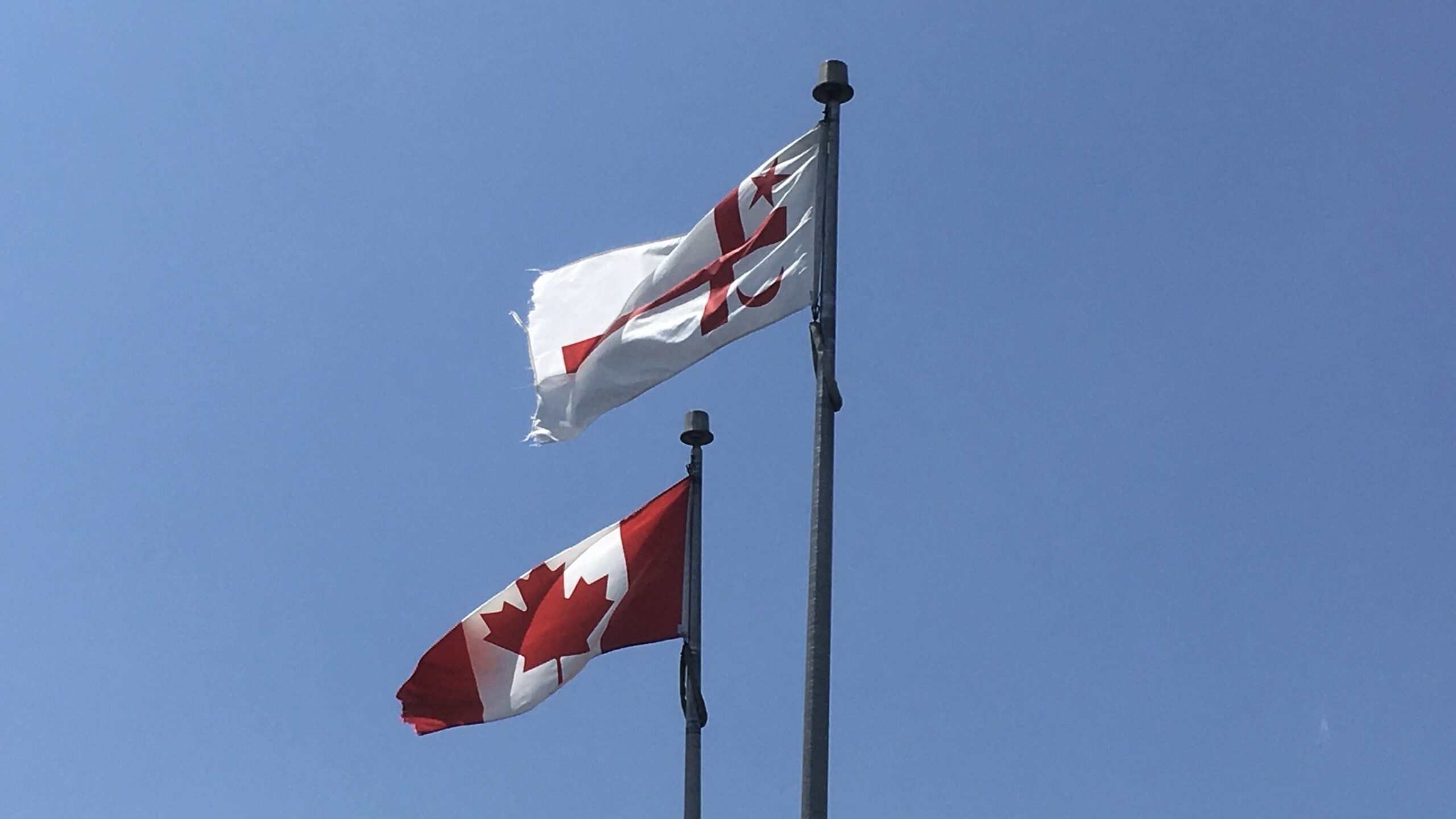 The Canadian flag and the Mi'kmaq Grand Council flag are bright against a cloudless blue sky.