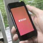 A man's hand holds a cellphone with the Tinder app open.