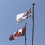The red and white Mi’kmaq Grand Council flag and the canadian flag against a clear blue sky.