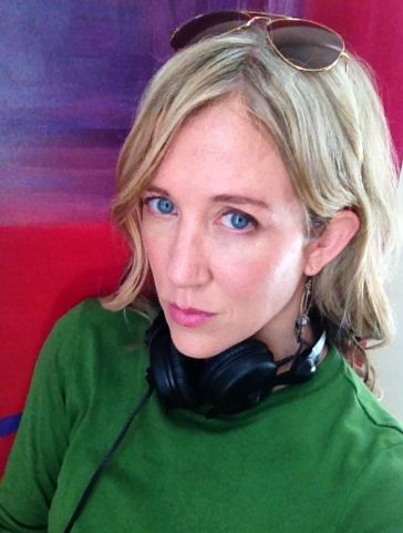 Headshot of blonde woman with shoulder length hair. She is wearing a green shirt and there is a blue and red background