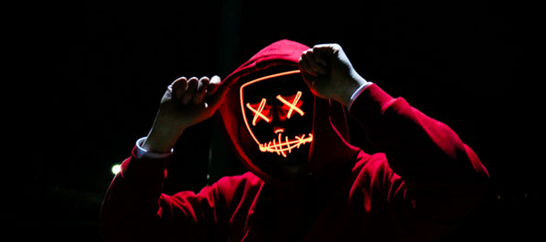 Cartoonish image of a figure in a red hoodie, gloved hands clenched into fists on either said of its head. The face is not visible, but orange lights, kind of like a jack-o-lantern show an x for each eye and a scar-like pattern for a mouth, with a small horizontal line for a nose.