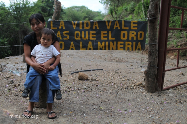 Angelina Noj from San Pedro Ayampuc in Guatemala holds her son Esmit in front of a banner at the blocked entrance gate to the Tambor gold mine. Photo: James Rodríguez