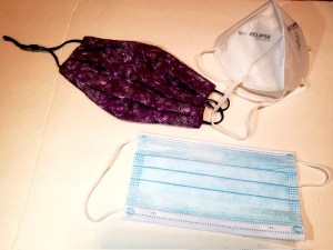 A display of a purple cloth mask, a white N95 respirator mask, and a blue surgical mask.