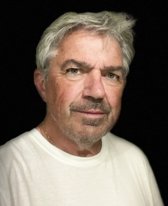 A headshot of a white man with silver hair and a moustache and beard