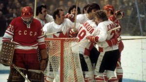 At a 1972 Canada-Russia hockey game, we see a Russian goalie in the forefront. Six Canadians hug each other behind the net in celebration.