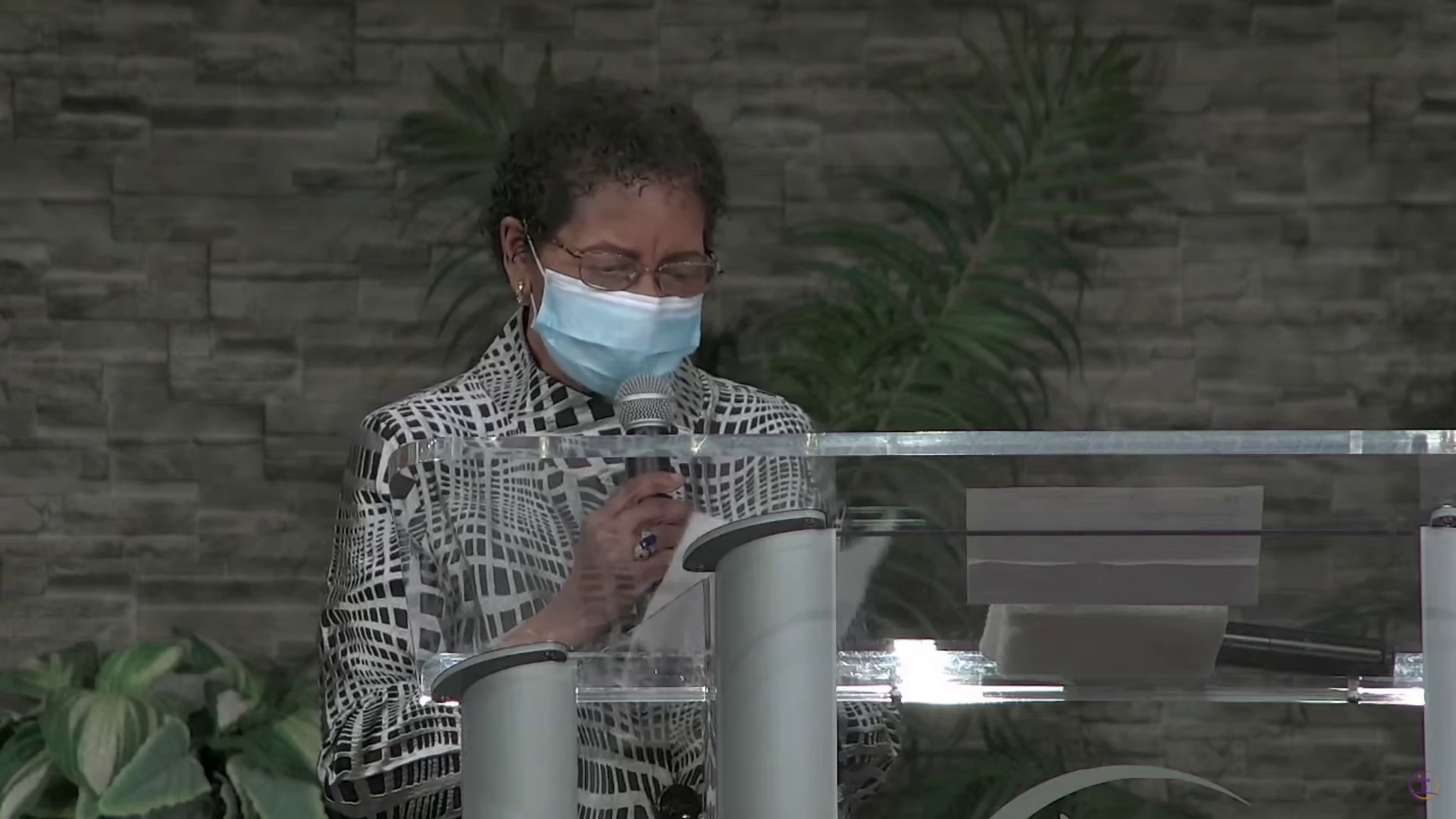 A woman wearing a blue medical mask speaks at a microphone at a church.