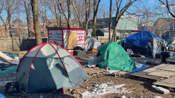 Four tents surround a temporary wooden shelter at People's Park. Some patches of snow on ground. It's daytime