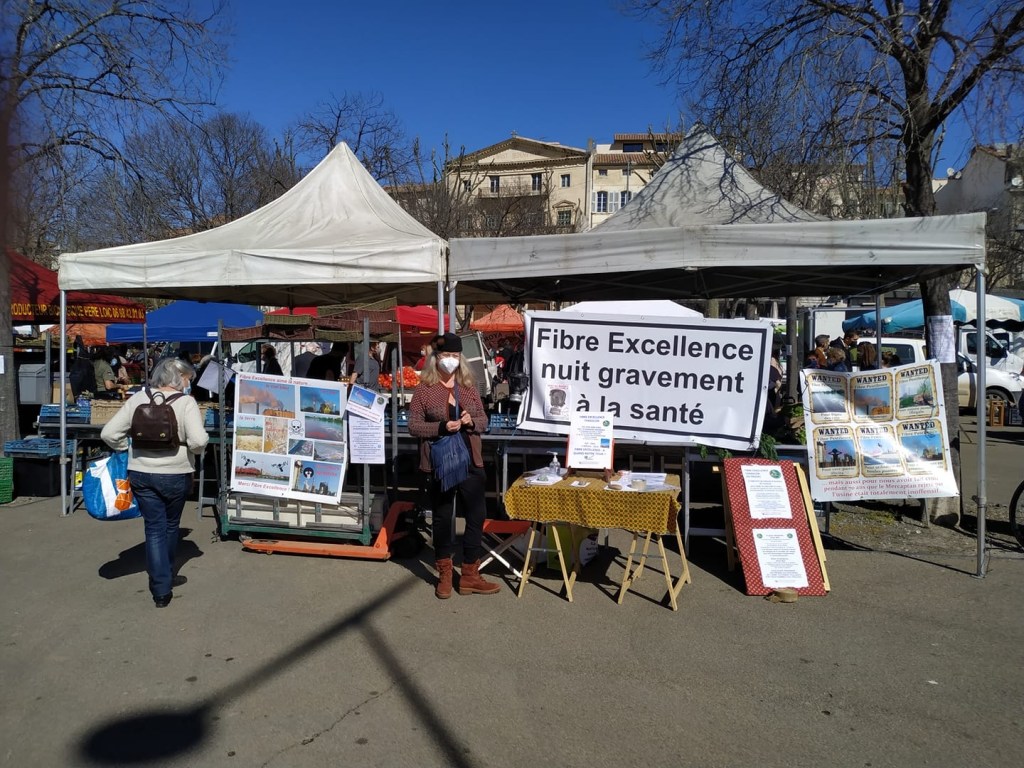 This photo shows Claire Simonin in front of a Flamants Roses du Trébon stand in the Arles market with a large banner saying in French Fibre Excellence seriously harms health, protesting the Paper Excellence mill in Tarascon, France. (contibuted)