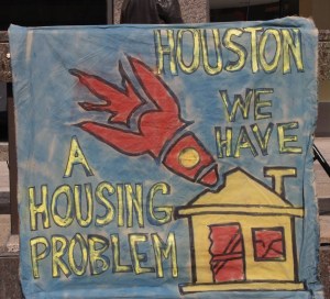 A painted protest sign that says Houston, we have a housing problem