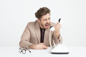 A man in a beige jacket yells into a white rotary phone