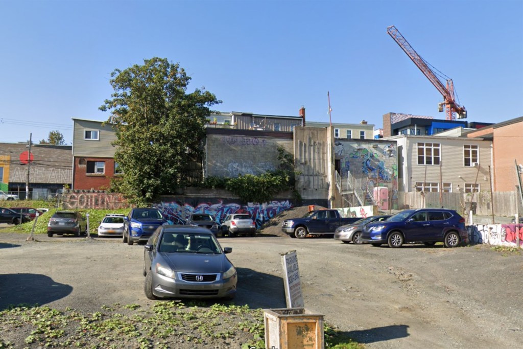 A screenshot of Google Streetview shows a gravel parking lot on a bright sunny day. In the background is a crane. In the middle, a few buildings are seen from the back. On the foundation of one of them, GOTTINGEN is written in white and red spray paint. There are a few vehicles in the parking lot.