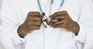 A close up of the chest of a doctor in a white lab coat holding a stethoscope.