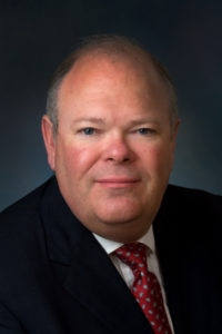 A middle aged bald man in a suit from the neck up. Portrait