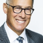 A white man with grey hair and a suit smiling broadly