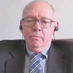 An older white man wearing a suit listening through headphones
