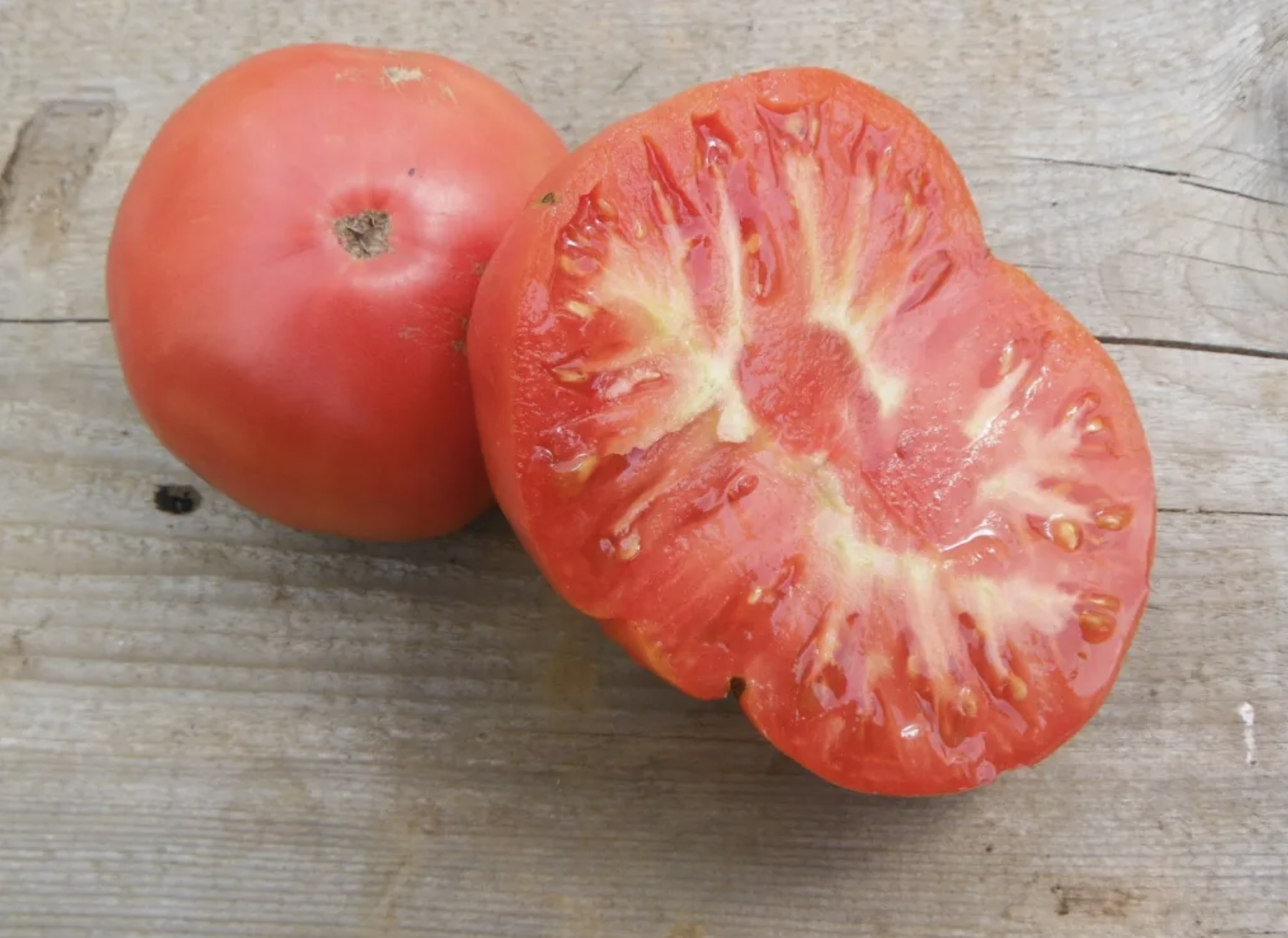 A freshly cut tomato sits on a wooden board.