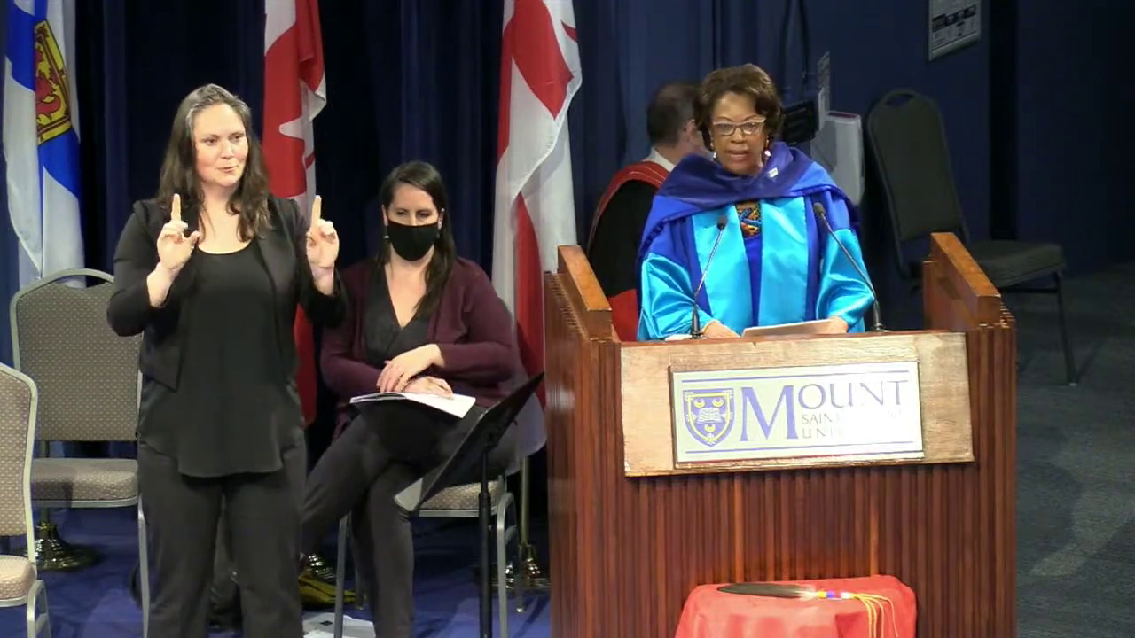 Black lady in blue graduation gown gives speech at a podium