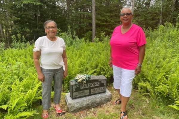 Two women stand in front of a glossy headstone in a cemetery
