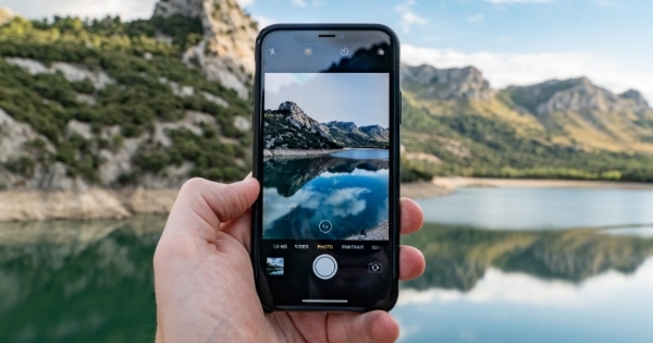 A man holding up a phone camera to a scene of a mountain reflecting on a clear lake