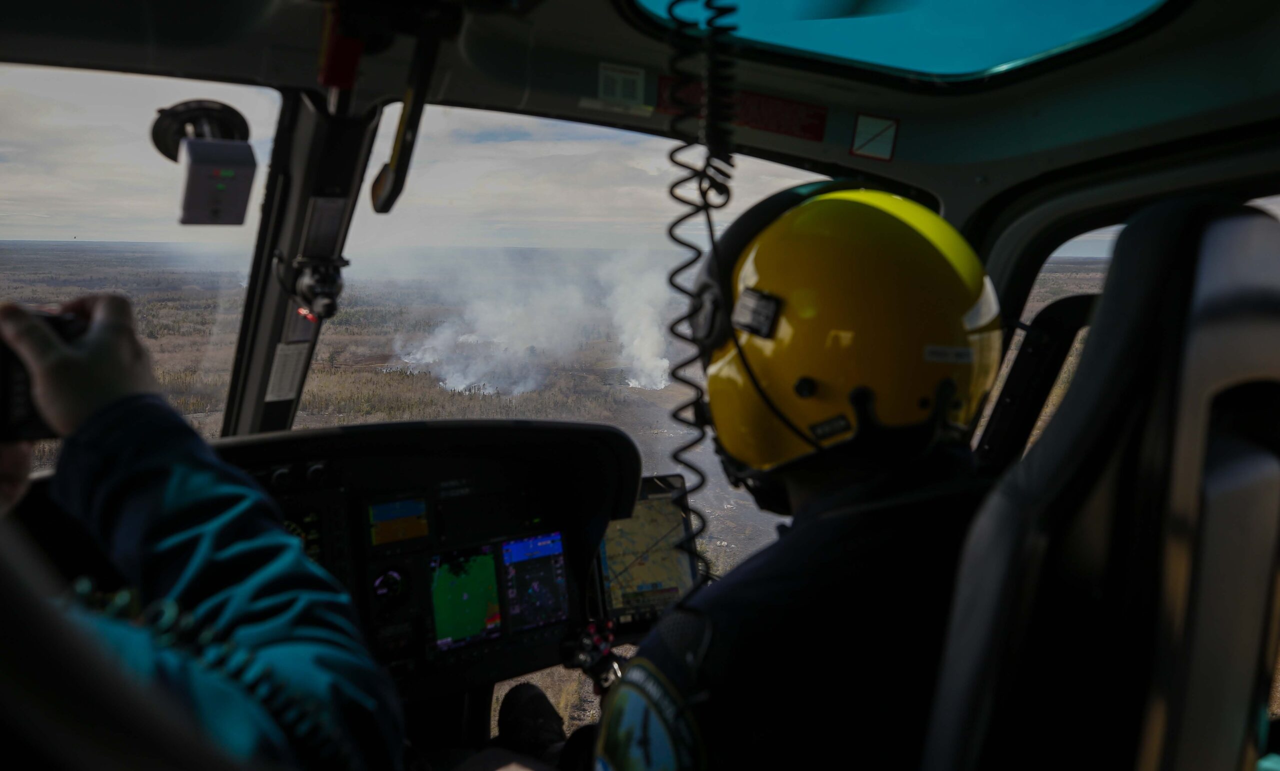 Helicopter cockpit picture of a pilot surveying forest fire smoke in the distance