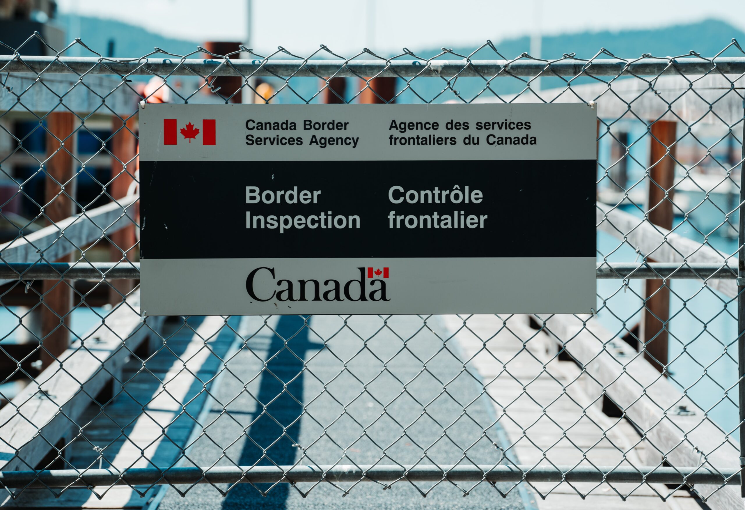 A sign for the Canadian border inspection attached to a chain link fence
