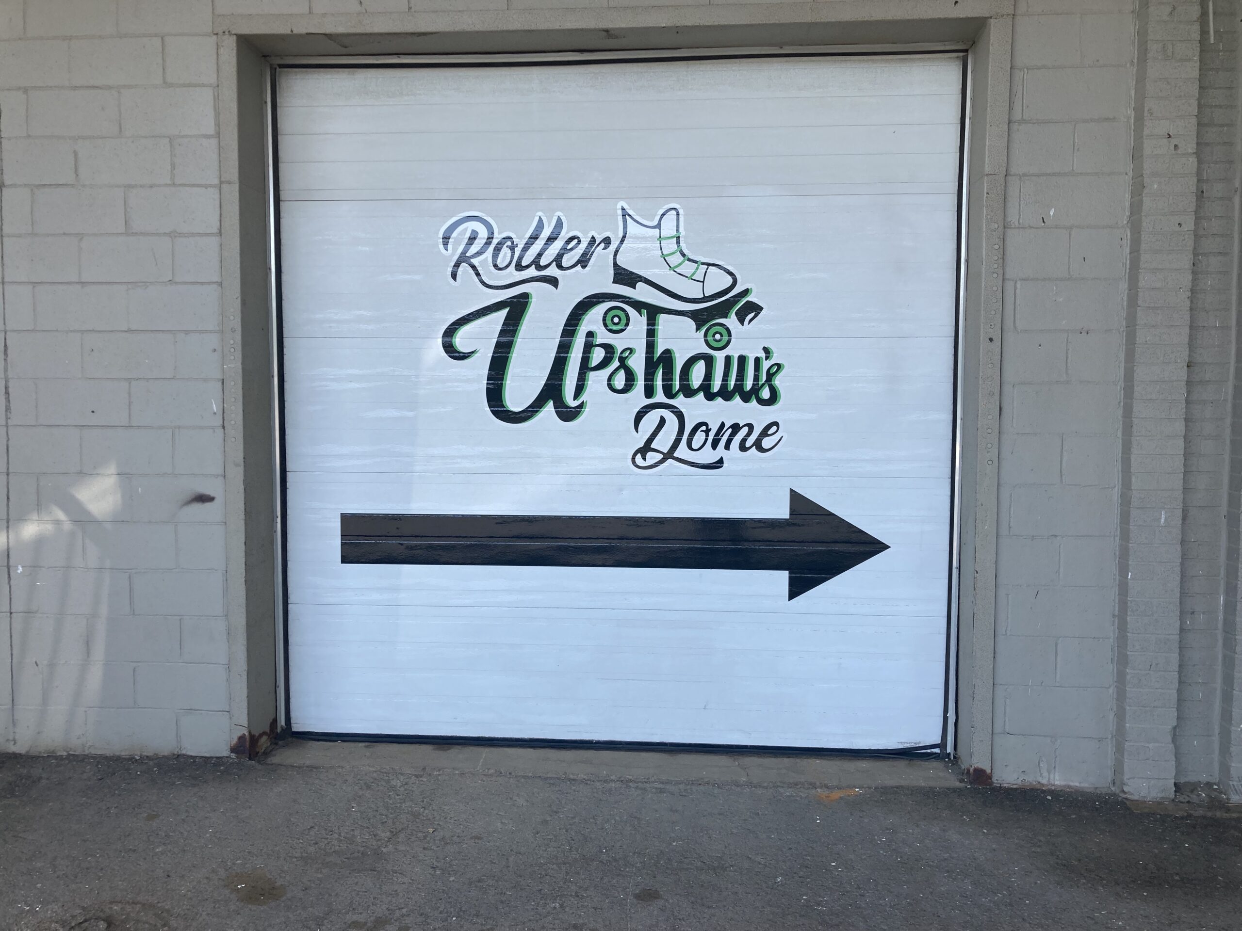 A white garage door painted with Upshaw's Roller Dome and an image of a roller skate. A black arrow at the bottom points to the roller dome's entrance.
