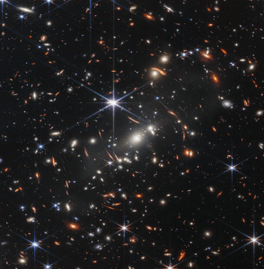 A cluster of galaxies, resembling swirling Christmas tree lights, against the black backdrop of space