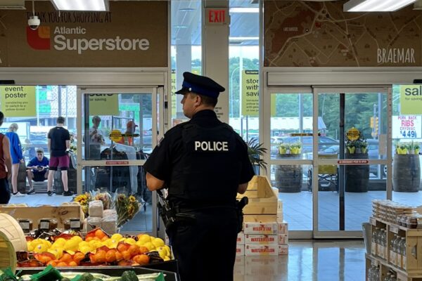 A uniformed police officer stands next to oranges and lemons near the entrance of a grocery store.